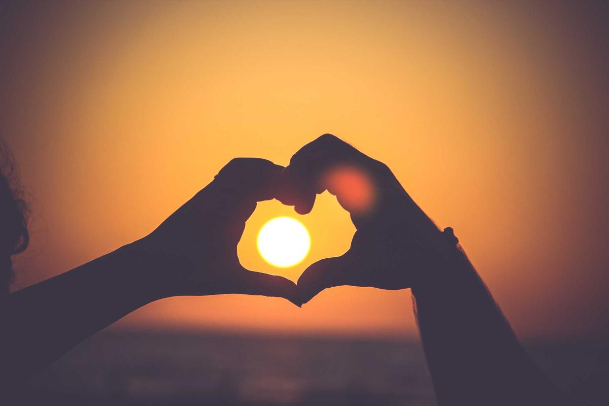 Hände formen ein Herz vor der Sonne